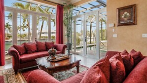 Un salon spacieux avec un canapé rouge, une table basse et une grande fenêtre donnant sur des palmiers et une piscine.