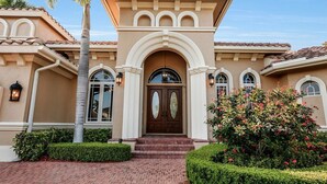 Une maison de style méditerranéen avec une entrée centrale, un chemin en briques et des jardins bien entretenus.