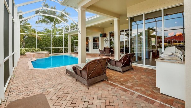A covered outdoor area with a pool, wicker furniture, and a grill station.