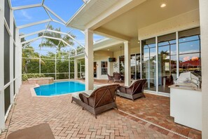 A covered outdoor area with a pool, wicker furniture, and a grill station. - SMARCO1255 3 Bedroom Holiday Home by Marco Naples Vacation Homes (Marco Island)