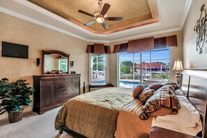 A bedroom with a large bed, a ceiling fan, a dresser, a TV, and a window with a view of a building and a pool. - SMARCO1255 3 Bedroom Holiday Home by Marco Naples Vacation Homes (Marco Island)