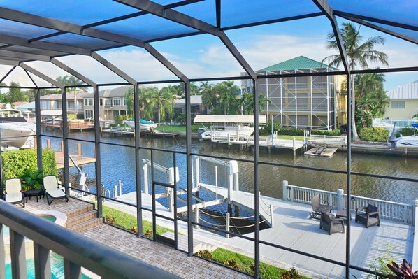 A view from a covered deck overlooking a marina with boats docked, a pool, and a building with scaffolding.