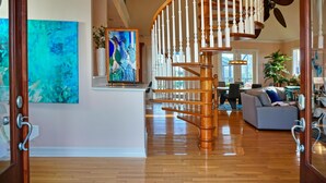 Uma sala ampla com escada de madeira, uma grande pintura abstrata e um sofá moderno.