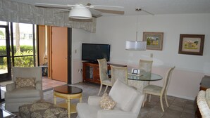A living room with a television, sofa, chairs, and a glass table.