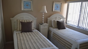 Two single beds with striped bedding, a bedside table with a lamp, and framed pictures on the wall. - Cove II 127F 2 Bedroom Condo By Midnight Cove II (Siesta Key)