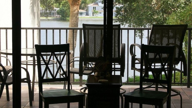 A balcony with chairs and a table, overlooking a body of water and houses. - Cove II 138F 2 Bedroom Condo By Midnight Cove II (Siesta Key)