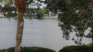 A lakeside view with a paved walkway, trees, and a distant building. - Cove II 138F 2 Bedroom Condo By Midnight Cove II (Siesta Key)