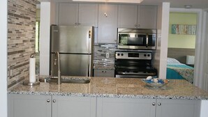 A modern kitchen with granite countertops, stainless steel appliances, and a recessed ceiling light. - Cove II 138F 2 Bedroom Condo By Midnight Cove II (Siesta Key)