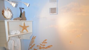 A bathroom with a sea-themed mural, a toilet, a sink, and a shelf with decorative items.