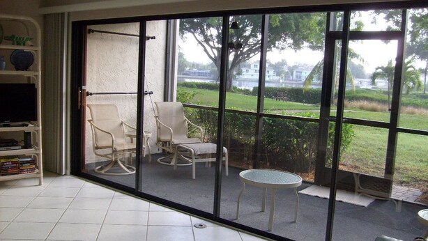 A room with a large sliding glass door leading to a balcony with outdoor furniture and a view of a green landscape.