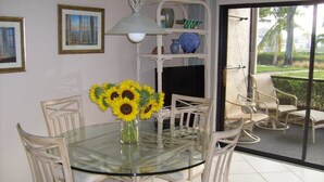 A dining area with a glass table surrounded by chairs, a vase with sunflowers, and a view of a garden through a sliding glass door.