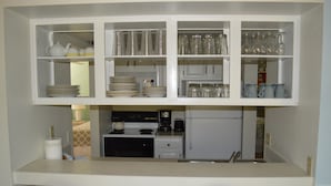 A compact kitchen with white cabinetry, a stove, a refrigerator, and a dining area with two chairs.