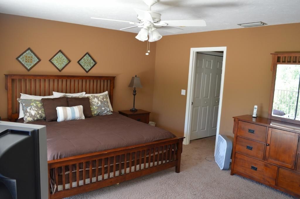 Une chambre à coucher comprenant un lit, une table de chevet, une commode, un ventilateur de plafond et des œuvres d’art décoratives murales.