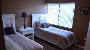 Un dormitorio con dos camas individuales, una mesita de noche con lámpara y una ventana con persianas.