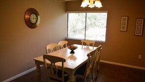 Un comedor con una mesa y sillas de madera, un reloj en la pared y una ventana con persianas.
