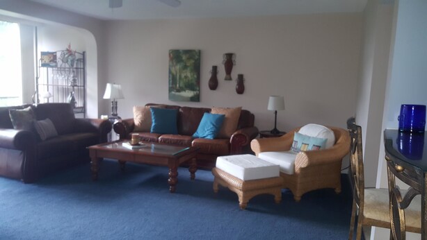 A living room with a blue carpet, two sofas, a coffee table, and a wicker chair. - Cove II 510F 2 Bedroom Condo By Midnight Cove II (Siesta Key)