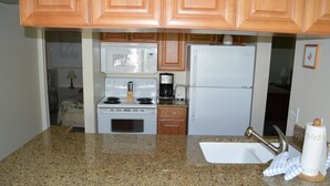 Una cocina con encimeras de granito, gabinetes de madera, estufa, microondas, tostadora y refrigerador.
