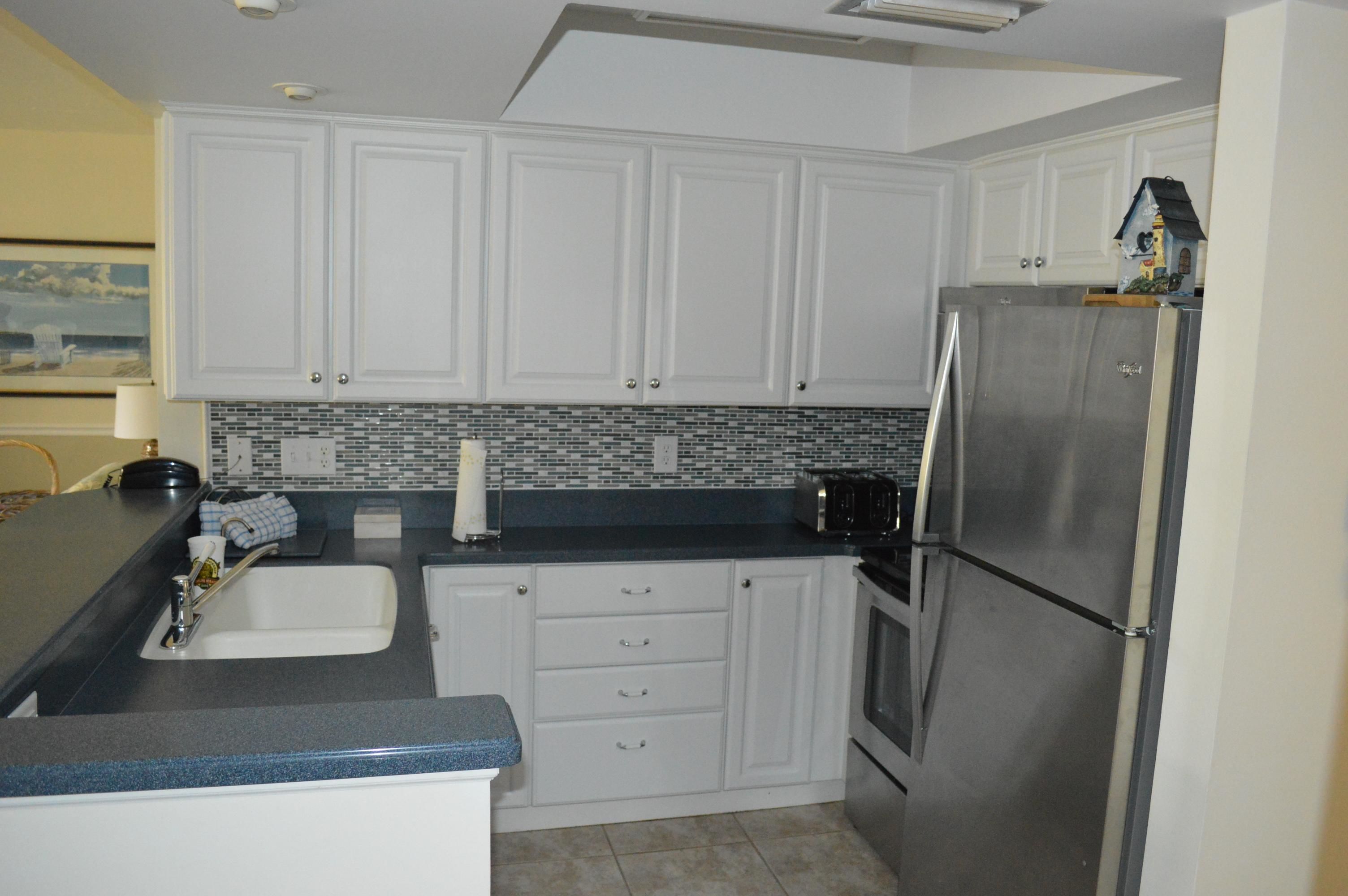 Una cocina con armarios blancos, un refrigerador de acero inoxidable y un salpicadero de azulejos.