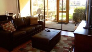 A living room with a sofa, ottoman, and a television. - Cove II 612F 2 Bedroom Condo By Midnight Cove II (Siesta Key)