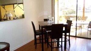 A dining area with a table and chairs, a lamp, and a view through a glass door to an outdoor patio. - Cove II 612F 2 Bedroom Condo By Midnight Cove II (Siesta Key)