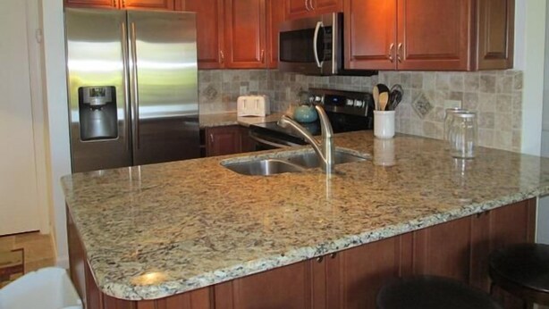 A kitchen with granite countertops, stainless steel appliances, wooden cabinets, and a built-in microwave. - Cove II 612F 2 Bedroom Condo By Midnight Cove II (Siesta Key)