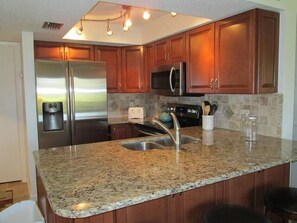 A kitchen with granite countertops, stainless steel appliances, wooden cabinets, and a built-in microwave. - Cove II 612F 2 Bedroom Condo By Midnight Cove II (Siesta Key)