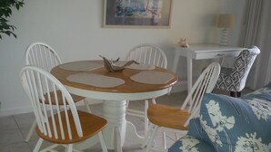 Un coin repas avec une table ronde, des chaises blanches et un canapé bleu recouvert d’un tissu à motifs floraux.