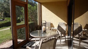 Eine verglaste Terrasse mit rundem Tisch und Stühlen, einer Tür, die nach draußen führt, und Blick auf einen Garten.