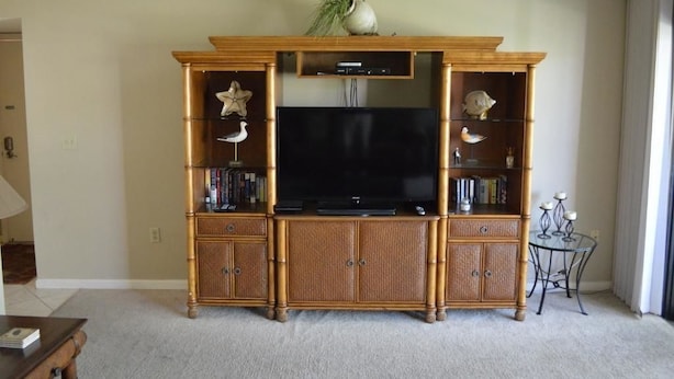 A living room with a wooden entertainment center, a flat-screen TV, and decorative items. - Cove II 620D 3 Bedroom Holiday home By Midnight Cove II (Siesta Key)