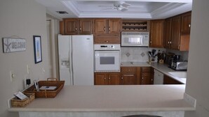 A kitchen with wooden cabinets, a white refrigerator, a microwave, an oven, and a coffee maker. There are two chairs at the kitchen island. - Cove II 620D 3 Bedroom Holiday home By Midnight Cove II (Siesta Key)