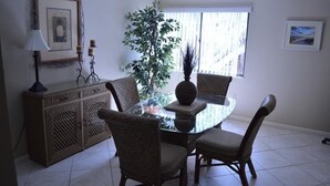 A dining area with a glass table surrounded by wicker chairs, a potted plant, and a decorative vase. - Cove II 620D 3 Bedroom Holiday home By Midnight Cove II (Siesta Key)