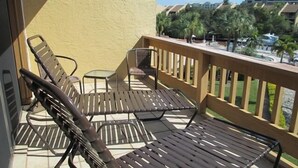 A balcony with two lounge chairs and a small table, overlooking a pool and palm trees. - Cove II 624D 3 Bedroom Holiday home By Midnight Cove II (Siesta Key)