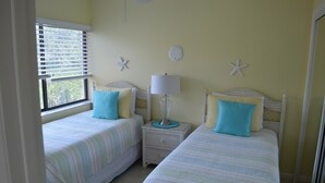 A bedroom with two beds, a nightstand with a lamp, and decorative starfish on the wall. - Cove II 633F 2 Bedroom Condo By Midnight Cove II (Siesta Key)