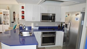 A modern kitchen with white cabinets, a blue countertop, stainless steel appliances, and a patterned rug. - Cove II 732F 2 Bedroom Condo By Midnight Cove II (Siesta Key)