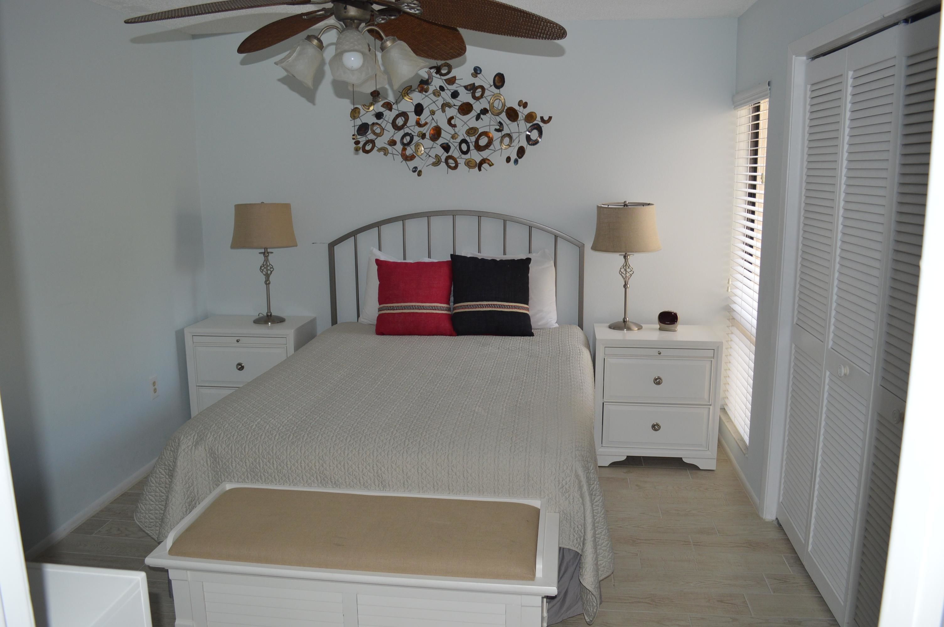 A bedroom with a bed, two bedside tables, a ceiling fan, and a window with blinds.