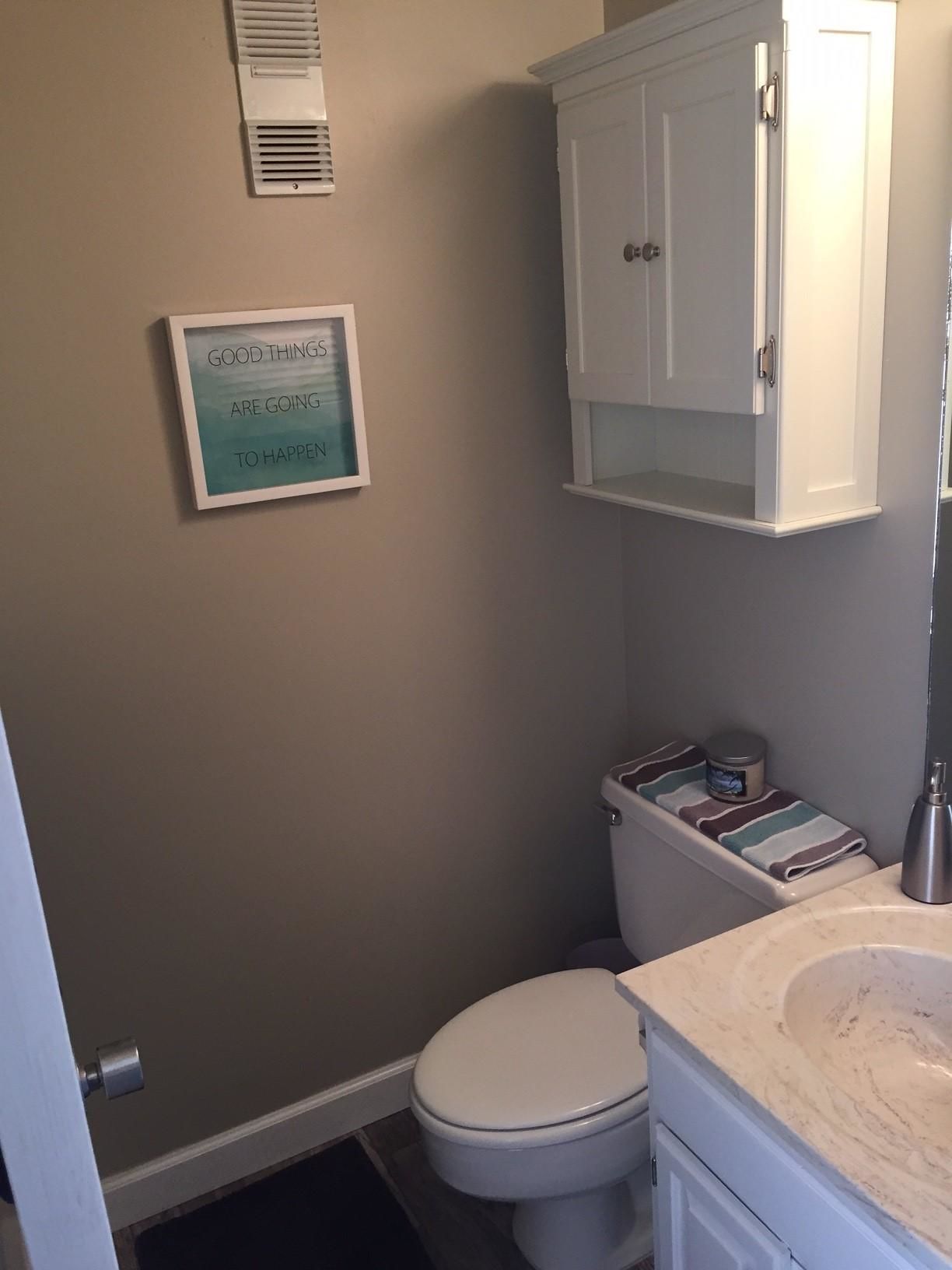 A bathroom with a toilet, a cabinet above the toilet, and a framed sign on the wall.