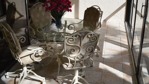 A sunlit patio with a glass table surrounded by ornate chairs, a ceiling fan, and a framed painting on the wall. - Cove II 811F 2 Bedroom Condo By Midnight Cove II (Siesta Key)