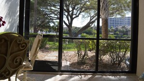 A room with a large window offering a view of a landscaped garden with trees and shrubs. - Cove II 811F 2 Bedroom Condo By Midnight Cove II (Siesta Key)