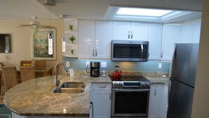 A modern kitchen with white cabinets, a built-in microwave, stainless steel appliances, and a skylight. - Cove II 811F 2 Bedroom Condo By Midnight Cove II (Siesta Key)