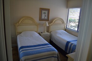 A room with two beds, each with a headboard and a bedside table with a lamp. There is a framed picture on the wall above the beds. - Cove II 811F 2 Bedroom Condo By Midnight Cove II (Siesta Key)
