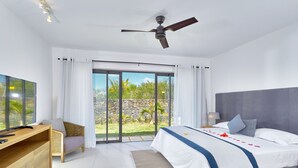 A modern hotel room with a large bed, a desk, a television, and a balcony with a view of greenery.