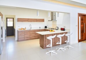 Une cuisine moderne avec des meubles en bois, un plan de travail blanc et trois tabourets de bar blancs.