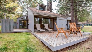 A modern cabin with a deck, outdoor seating, and a stone chimney.