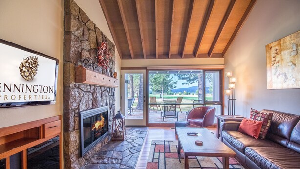 A spacious living room with a stone fireplace, leather sofa, and a dining area with a view of the outdoors.