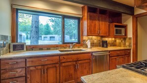 A kitchen with wooden cabinets, a stainless steel dishwasher, a microwave, and a large window with a view of trees and buildings.