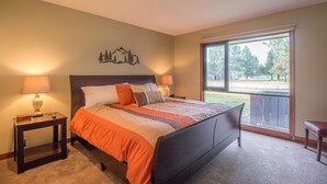 A bedroom with a large bed, two bedside tables with lamps, a window with a view of trees, and a wall-mounted decoration of trees.