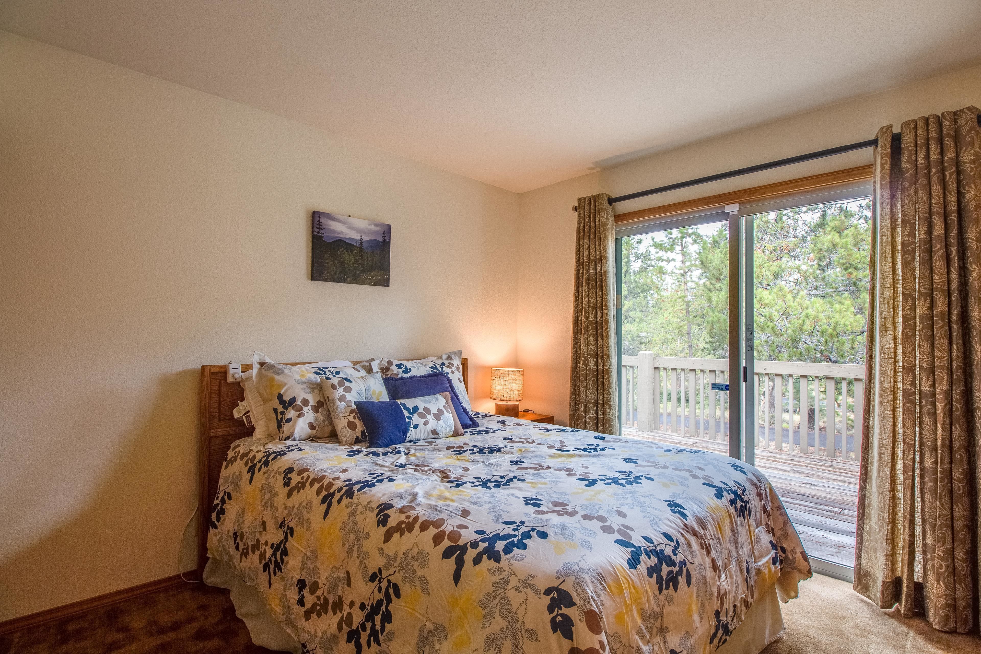 Une chambre avec un grand lit, une table de chevet, une lampe et une vue sur une terrasse accessible par une porte-fenêtre coulissante.