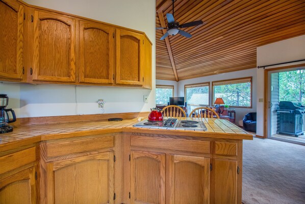 A kitchen with wooden cabinets, a central island with a kettle, and a ceiling fan.