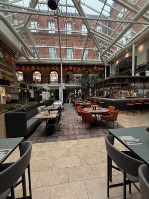 A spacious indoor area with a high ceiling and large windows, featuring seating areas, a bar, and a staircase leading to an upper level. - Hotel Alte Post Flensburg (Flensburg)
