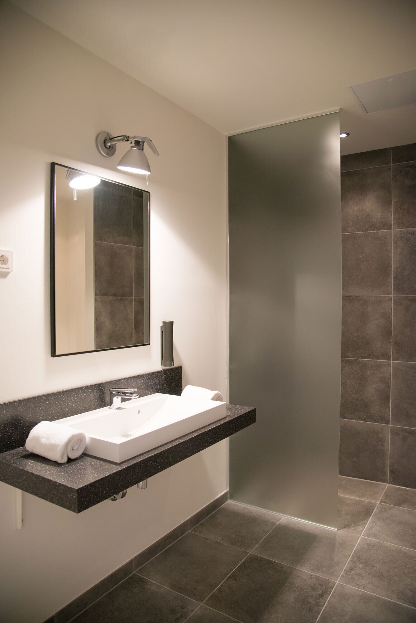 Un baño moderno con un espejo grande, un lavamanos blanco y una zona de ducha.
